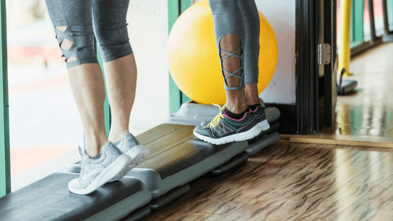 Fötter och vader på stepbrädor i gym – ena hälen lyft