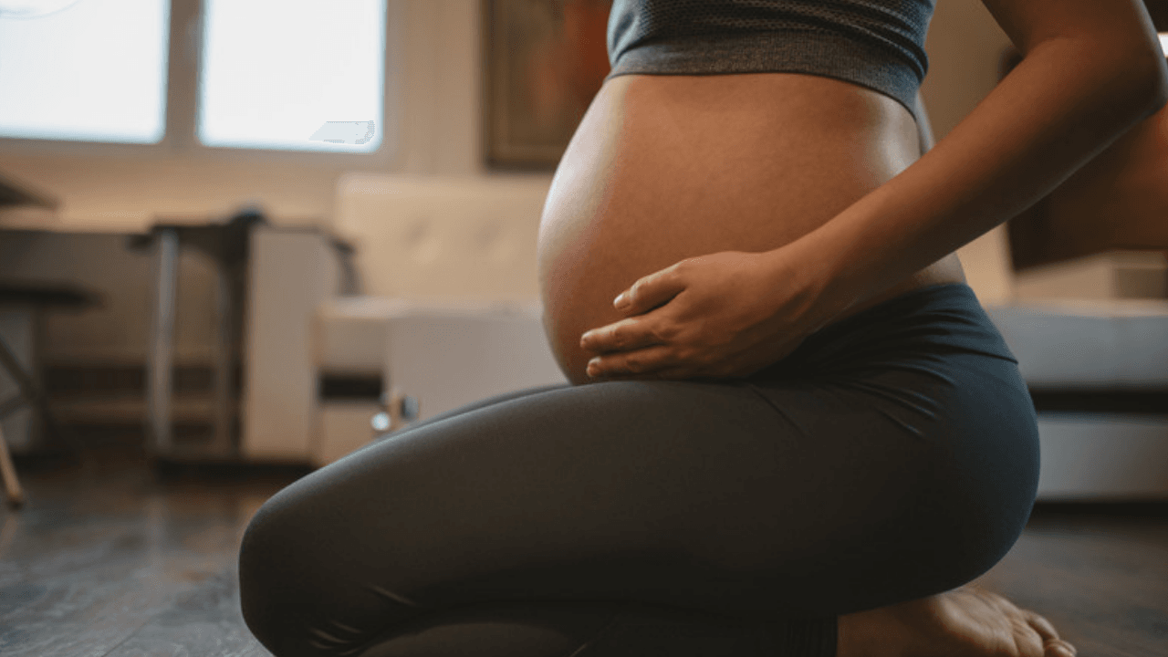 Gravid kvinna sitter på golvet med händerna på magen