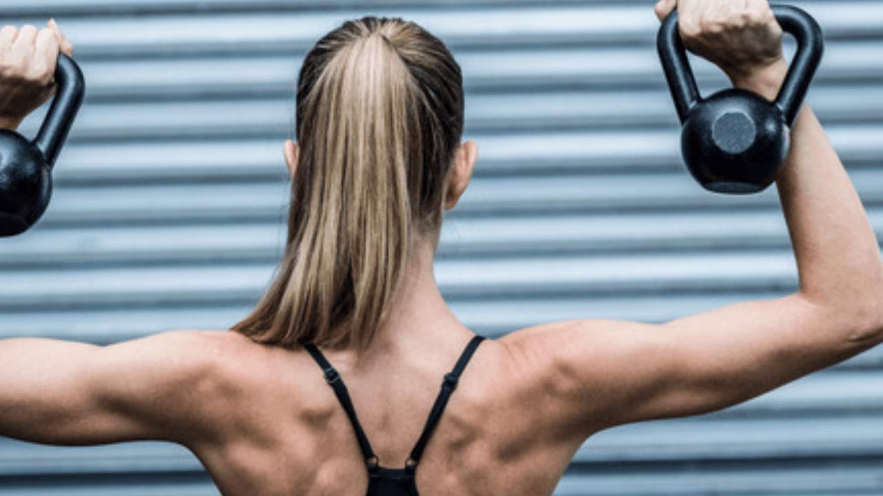 Kvinna sedd bakifrån håller två kettlebells i axelhöjd