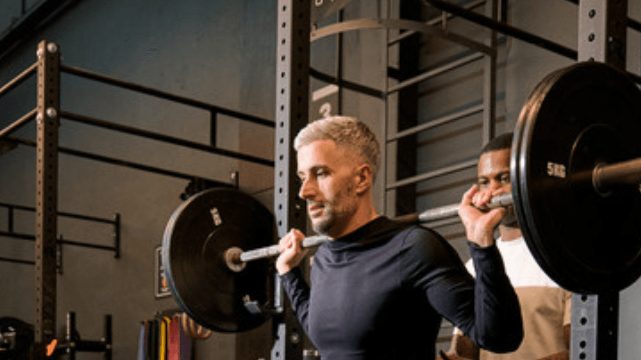 Man med skivstång i power rack, träningspartner bredvid