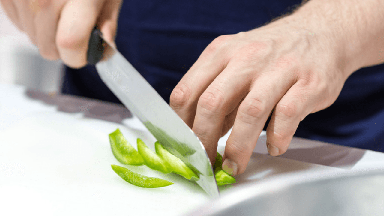Händer skär grön paprika på skärbräda
