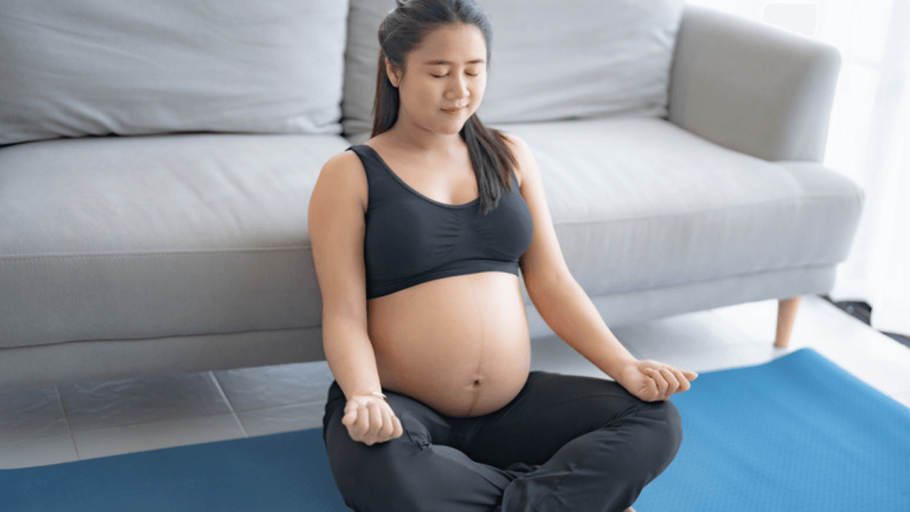Gravid kvinna sitter i skräddarställning på yogamatta