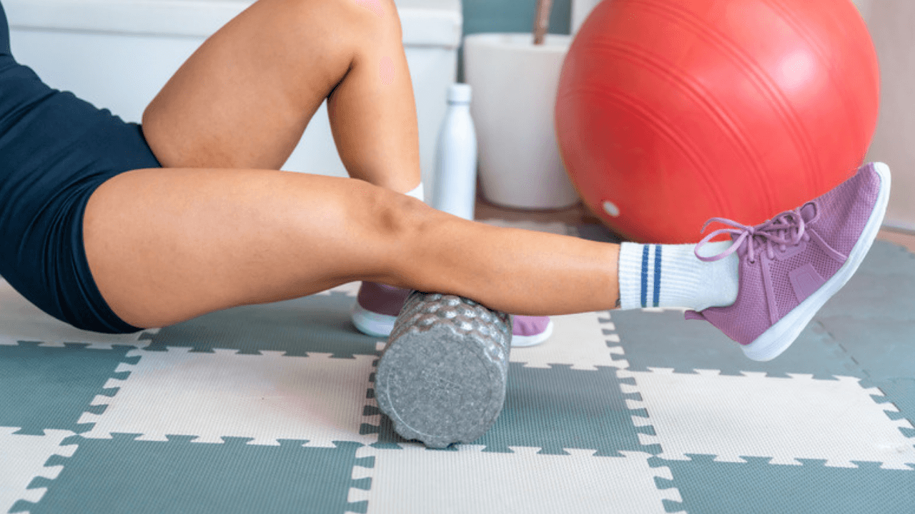 Kvinna rullar vaden på foamroller på träningsgolv