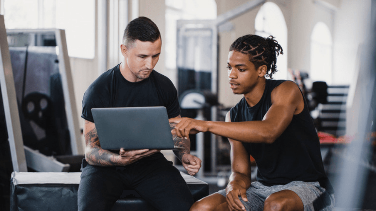 Ung kille sitter på gymbänk och får instruktioner av tränare
